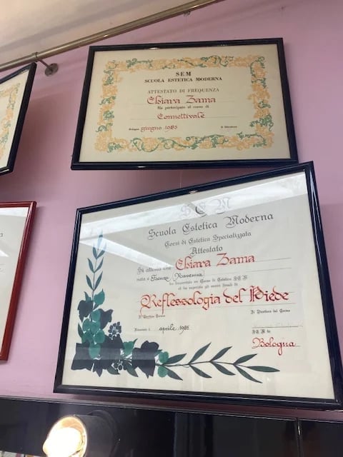 Two framed Italian diplomas mounted on a pink wall